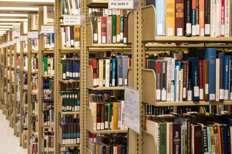 Corredor entre estantes altas repletas de livros em biblioteca