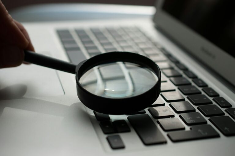 Lupa sobre documentos ao lado de notebook em análise investigativa